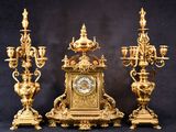 une horloge en or posée sur une table, à côté de trois chandeliers