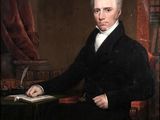 portrait of a man in a black suit sitting at a desk