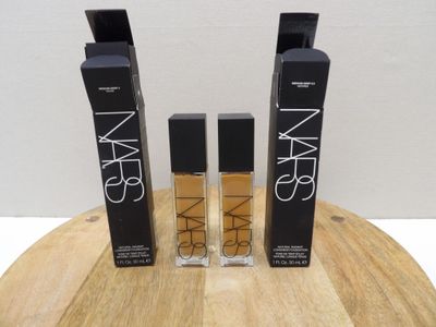 trois flacons de produits cosmétiques Nars posés sur une table en bois