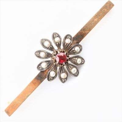une broche en forme de fleur, argentée et rouge, ornée de perles et fixée sur une tige en bois