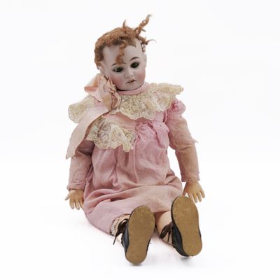 an old doll sitting on the ground wearing a pink dress and brown shoes
