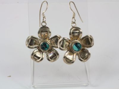silver flower earrings with green stones on a clear acrylic stand