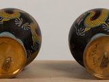 pair of black and gold vases with dragon designs on them sitting on a table