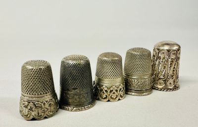 six antique thimbles lined up in a row on a white surface