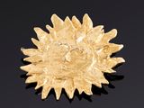 une image représentant une broche en forme de tournesol doré posée sur une surface noire