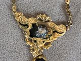 a close up of a gold necklace with a black stone on it