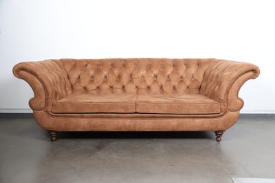 an image of a tan leather couch sitting on top of a cement floor