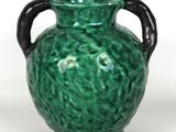 a green vase with a black handle on a white surface