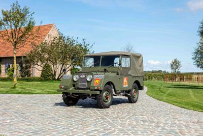a green jeep parked on a cobblestone road in front of a house