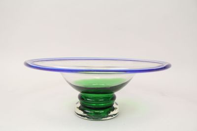 un bol en verre vert bordé de bleu, posé sur un socle