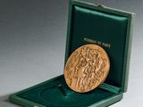 l'image d'une médaille d'or dans une boîte verte posée sur une surface grise