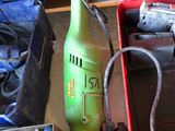 une perceuse électrique verte posée sur une table à côté d'autres outils