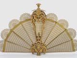 an antique gold fan with intricate designs on it on a white surface