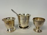 three silverplated cups and a spoon on a white surface