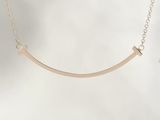 a close up of a gold necklace with a curved bar on a chain