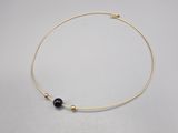 un collier plaqué or orné d'une perle noire sur un fond blanc