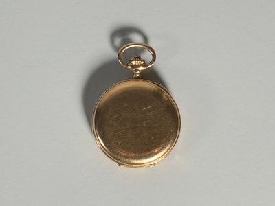 une petite montre de poche en or posée sur une surface blanche