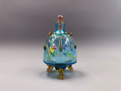 une image représentant un flacon de parfum en verre bleu orné de fleurs