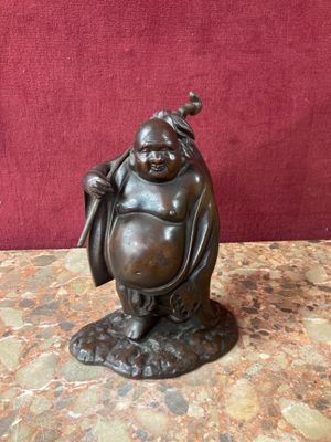 bronze statue of a laughing buddha holding a bag on a table