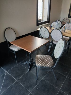 Dans un restaurant au sol carrelé de noir, des tables et des chaises sont alignées.