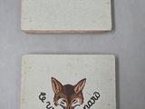 deux dessous de verre ornés d'une image de renard, posés sur une table