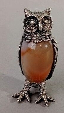 une figurine de chouette sur laquelle est posée une pierre orange, entre ses pattes