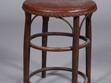 un vieux tabouret en bois avec une assise en cuir, sur fond gris