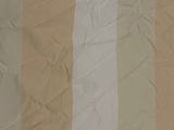 beige and white striped fabric on a bed with a white pillow