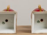 two white vases with red apples in them on a table
