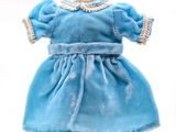 robe bleue pour une poupée posée sur un socle en bois, sur fond blanc