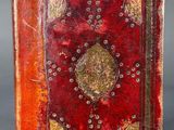 an old book with a red cover and gold trim