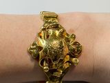 gold plated bracelet with a skull and flowers on a woman ' s arm