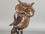 figurine de chouette en argent et en or, perchée sur un rocher, sur fond gris