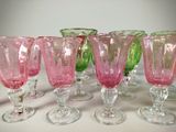 several pink and green glass goblets are lined up on a table