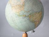 un petit globe terrestre posé sur un socle en bois, sur fond blanc