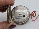 a person holding a silver pocket watch with a red string