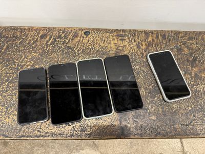 Plusieurs téléphones portables sont alignés sur une table devant un mur blanc.