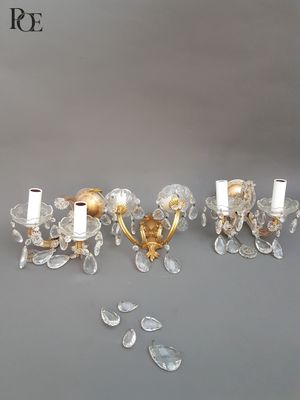 three crystal and brass wall sconces on a grey background