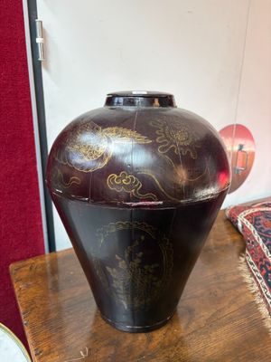 un vase noir posé sur une table en bois, avec un mur rouge en arrière-plan