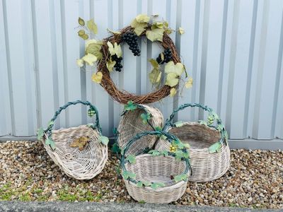 trois paniers en osier garnis de raisins et de feuilles, posés sur du gravier