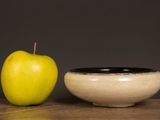 a yellow apple next to a black bowl on a table