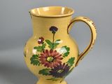 a yellow vase with flowers on it on a gray surface