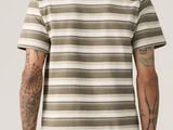 a man wearing a striped t - shirt and jeans standing in front of a white wall