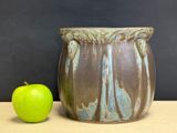 a green apple next to a brown vase on a table