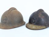 Deux vieux casques de pompier sont posés sur une surface blanche