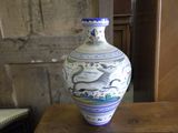 a vase sitting on a wooden table with a painting on it