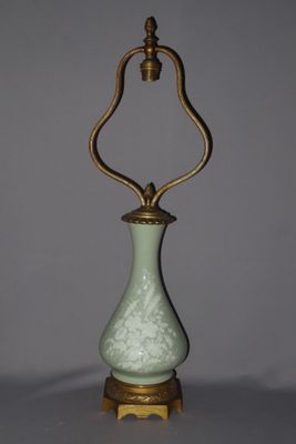 a green vase with a gold handle sitting on top of a table