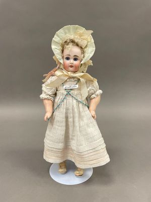 une poupée ancienne en porcelaine représentant une jeune fille vêtue d'une robe et d'un bonnet