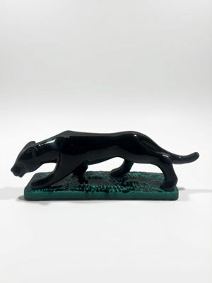 une figurine de chien noir posée sur un socle vert, sur fond blanc
