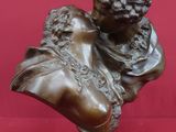 un buste antique en bronze représentant un homme tenant un oiseau, sur fond rouge